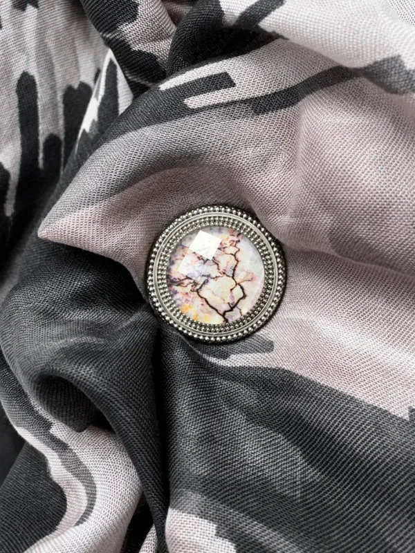 Dena Lyons silver magnetic scarf pin featuring original marble-inspired artwork beneath beveled crystal, elegantly securing a black and blush patterned scarf.